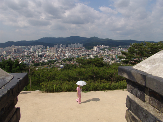 수원이 한눈에 들어오는데 양산을 쓰고 지나가는 여성이 돋보인다. 멀리 화성이 보인다 